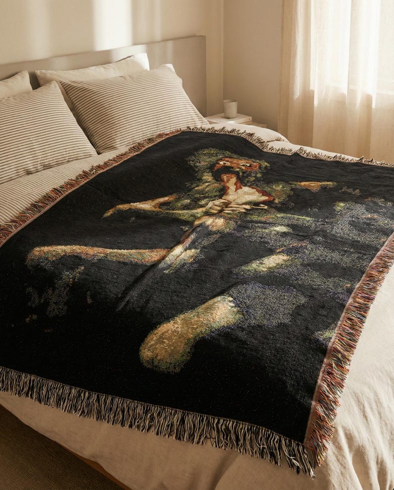 Pu&ograve; includere: Una coperta in tessuto nero con una dettagliata rappresentazione artistica multicolore di una figura con un'espressione dagli occhi sgranati. La coperta rettangolare presenta una superficie testurizzata e bordi con frange.