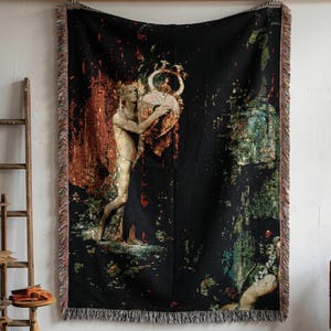 May include: A rectangular woven throw blanket featuring a black background with a central illustration of a figure holding a large vessel. The design incorporates warm orange, red, and cool green tones with fringed edges on all four sides.