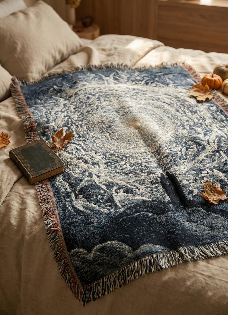 May include: A rectangular woven throw blanket featuring a dark blue and cream intricate celestial pattern with a central sunburst design, finished with fringed edges on all sides, displayed on a neutral-coloured bedspread.