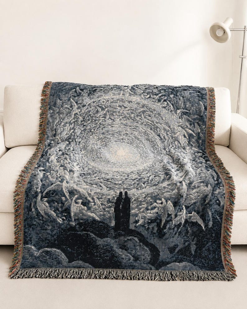 May include: A woven throw blanket featuring a dark blue and white tapestry design of two figures standing on a rocky cliff looking towards a bright, swirling celestial light surrounded by winged forms, finished with a fringed edge.