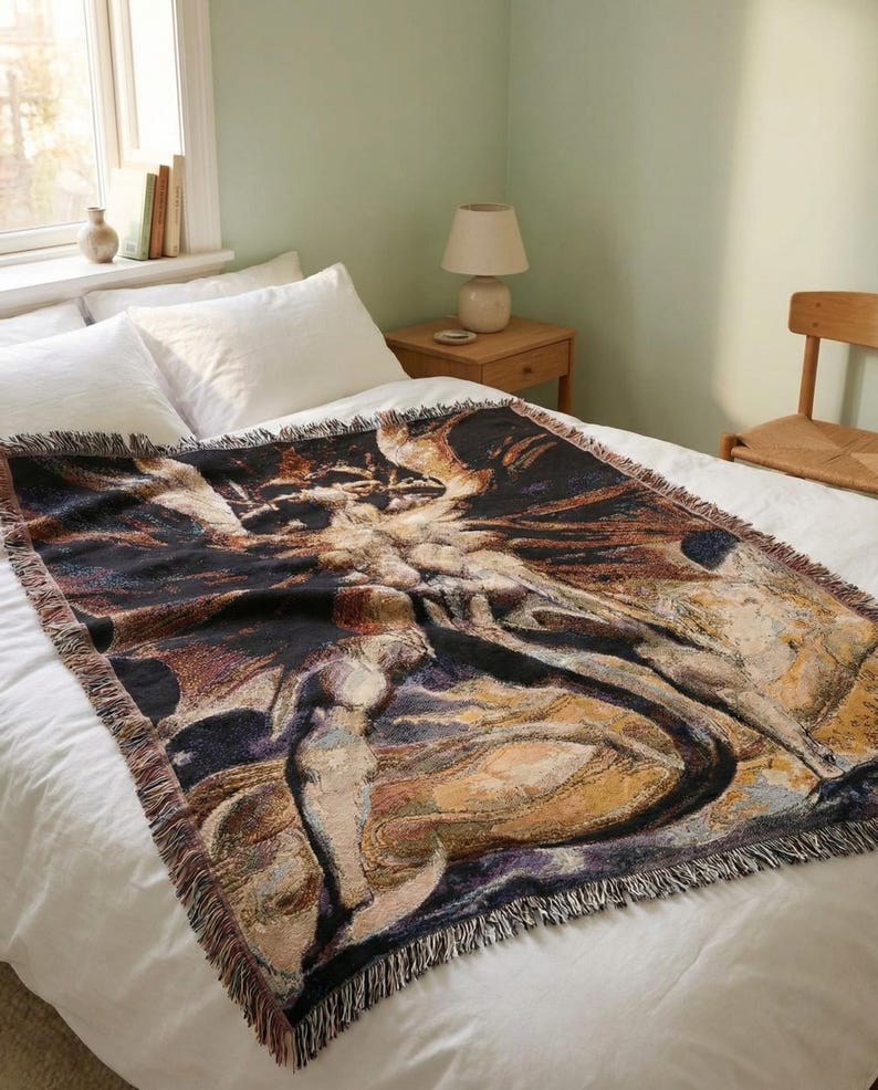 Puede incluir: Una manta tejida rectangular con un dise&ntilde;o art&iacute;stico oscuro y complejo en tonos negro, dorado y crema. La manta tiene bordes con flecos y est&aacute; extendida sobre una colcha blanca, mostrando un patr&oacute;n detallado y multicolor.