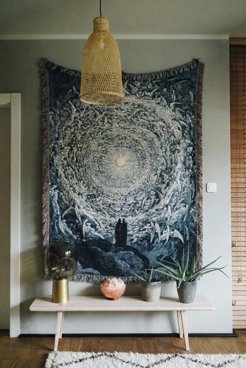 May include: A rectangular woven wall tapestry featuring a dark blue and cream circular celestial design with a central light source and two silhouetted figures standing on a rocky landscape at the bottom, finished with fringed edges.