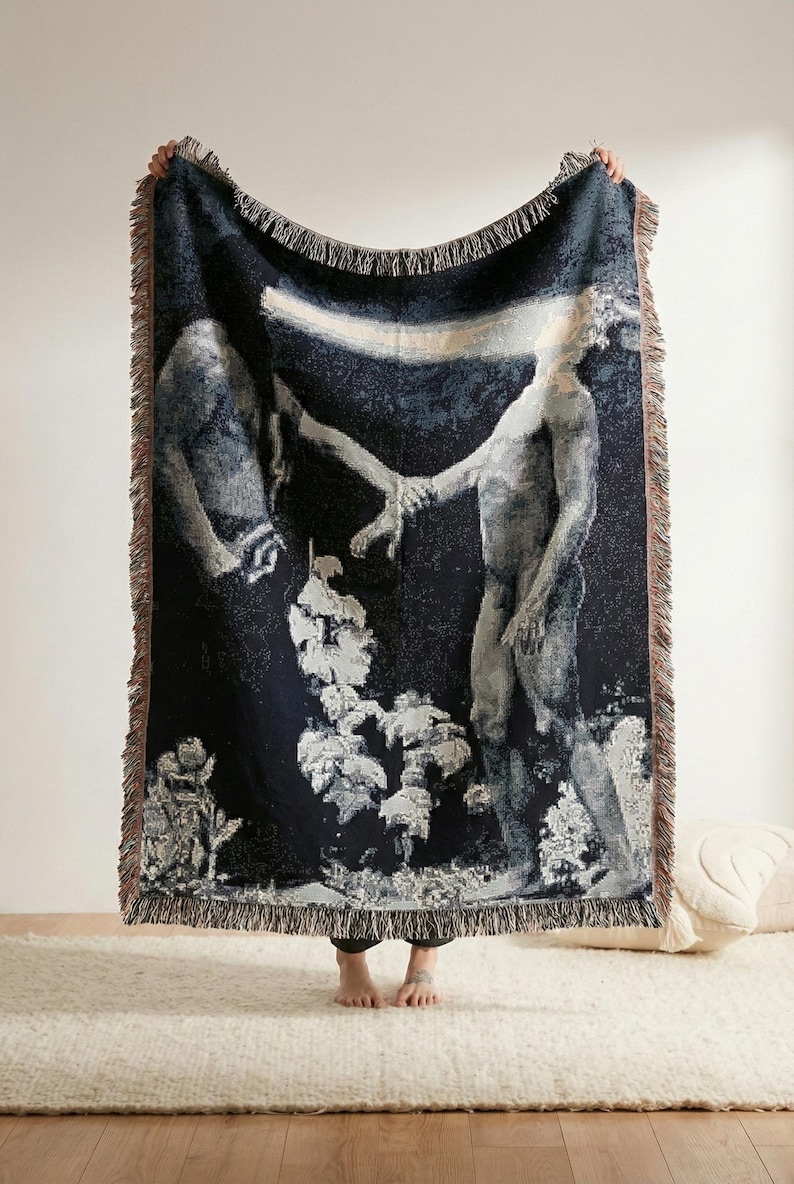 May include: A woven throw blanket featuring a dark blue background with a graphic illustration of two figures reaching toward each other, connected by a horizontal beam of light, finished with a fringed edge on all four sides.