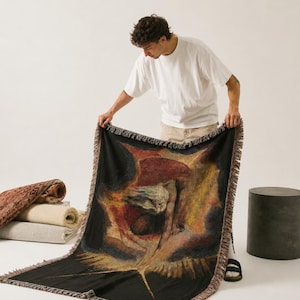Puede incluir: Una manta tejida rectangular que presenta una reproducci&oacute;n de la pintura The Ancient of Days de William Blake. La obra muestra una figura que extiende un comp&aacute;s hacia abajo sobre un fondo oscuro y ardiente. La manta tiene bordes con flecos.