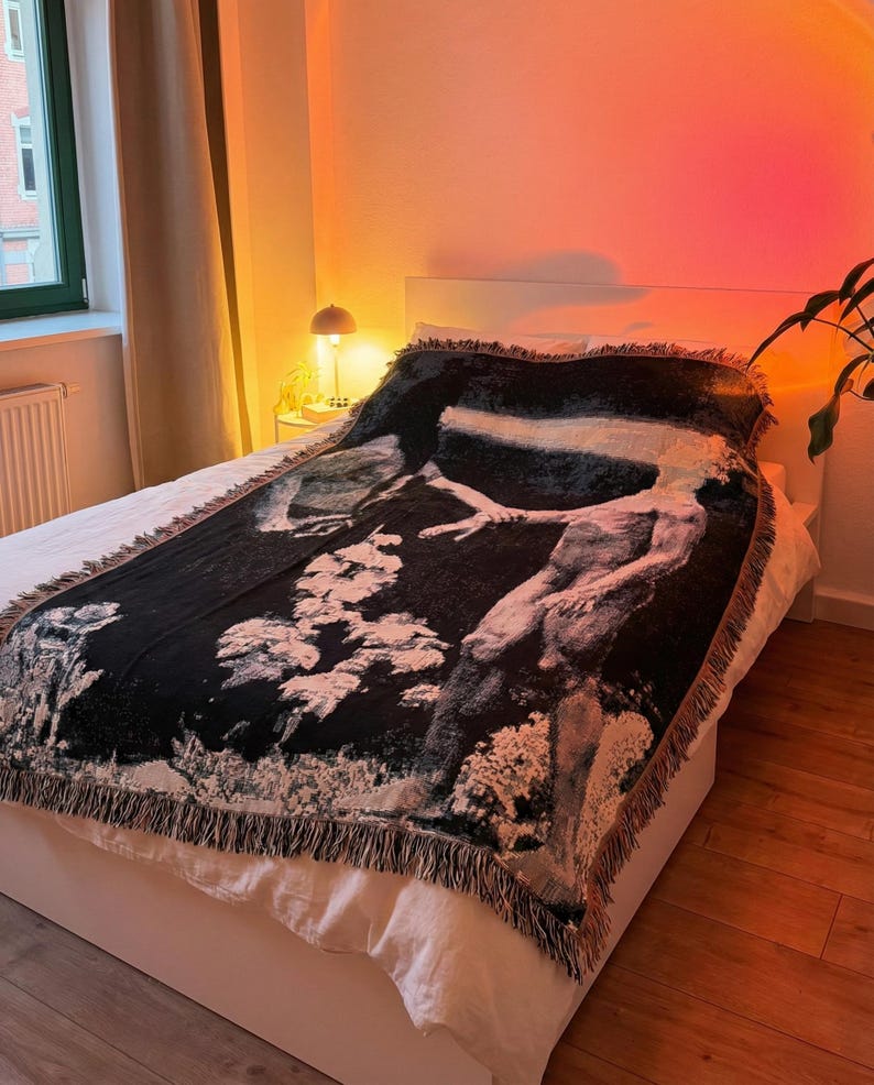 May include: A rectangular woven throw blanket featuring a high-contrast black and white graphic design of a human figure reaching out amidst textured, cloud-like shapes. The blanket has a decorative fringed edge along all four sides.