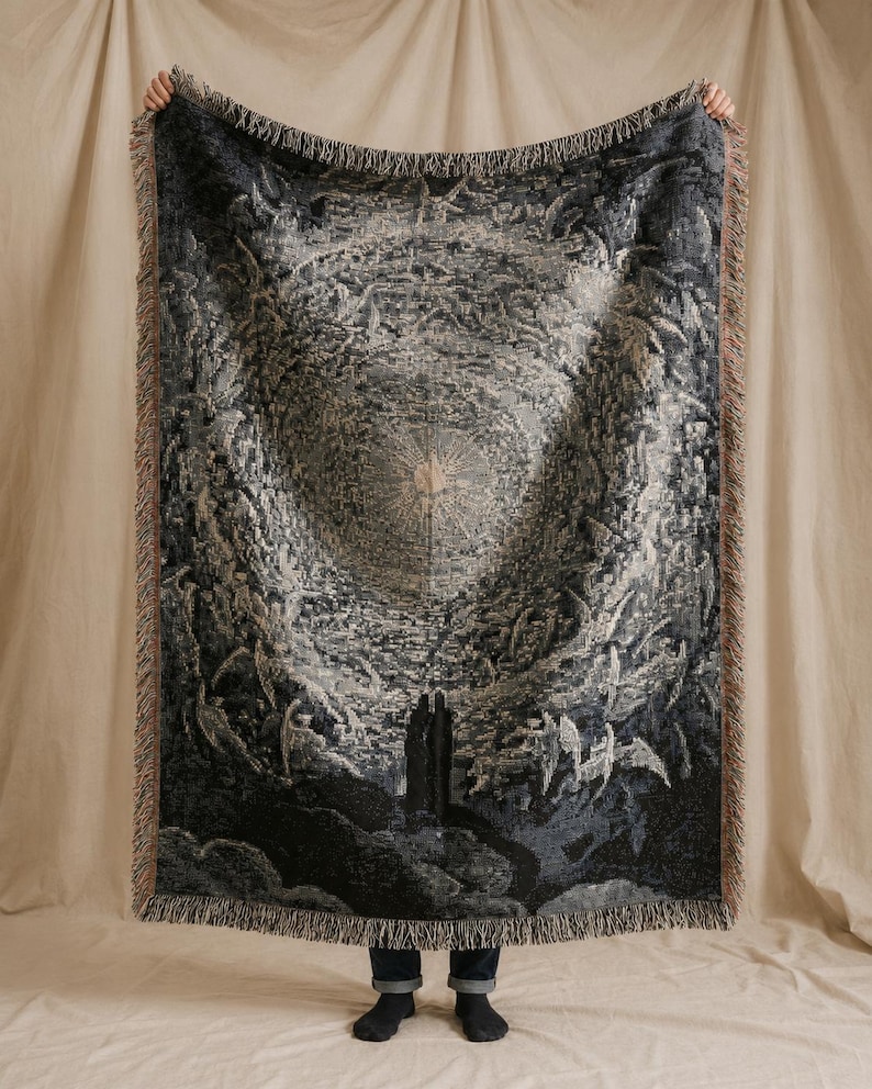 May include: A rectangular woven throw blanket featuring a detailed monochromatic illustration of a celestial scene with a central radiating light source, dark swirling clouds, and two figures standing at the bottom, finished with fringed edges.