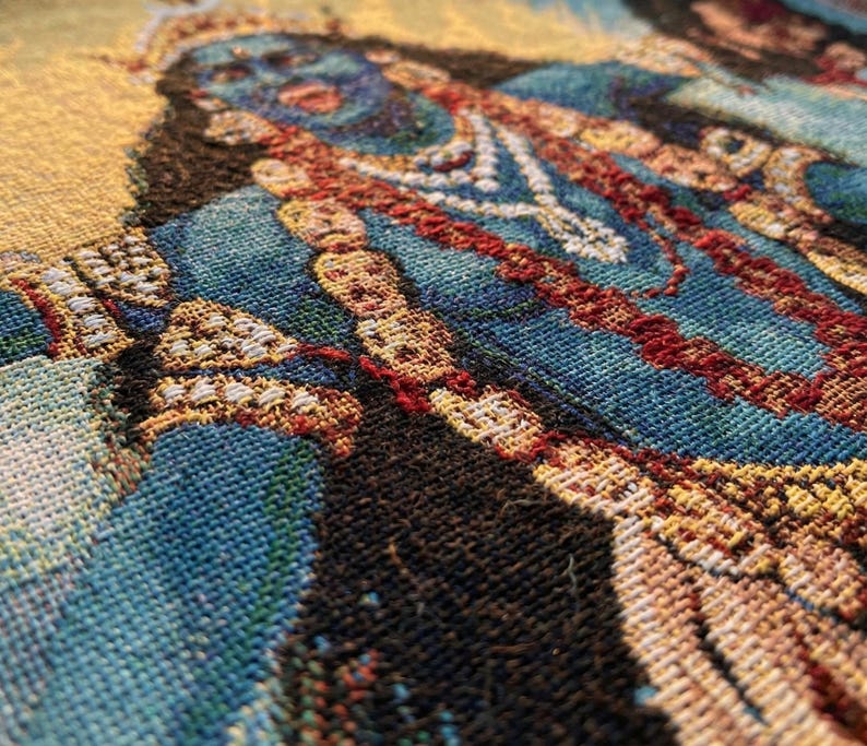 K&ouml;nnte beinhalten: Ein gewebter Wandbehang mit einer detaillierten Darstellung einer blauh&auml;utigen Figur, die mit geschichteten Halsketten und verziertem Schmuck geschm&uuml;ckt ist. Der Stoff zeigt eine reiche Farbpalette aus tiefem Blau, leuchtendem Gelb und Dunkelbraun.