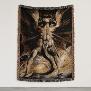 Puede incluir: Una manta tejida que presenta una ilustraci&oacute;n oscura y detallada de una figura alada y musculosa con cola, sobre un fondo negro con reflejos de color marr&oacute;n dorado y un borde decorativo con flecos en los cuatro lados del tejido rectangular.