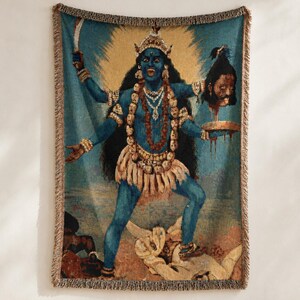 K&ouml;nnte beinhalten: Eine gewebte Wohndecke mit einer blauh&auml;utigen Figur mit mehreren Armen, die eine Krone und eine Totenkopfkette tr&auml;gt. Die Figur h&auml;lt ein Schwert und einen abgetrennten Kopf &uuml;ber einer Schale und steht auf einer liegenden Figur, mit Fransen an den R&auml;ndern.