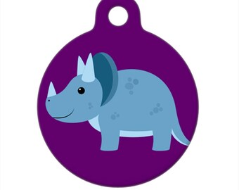 Può includere: Un'etichetta rotonda per animali domestici di colore viola con un triceratopo blu in stile cartone animato.