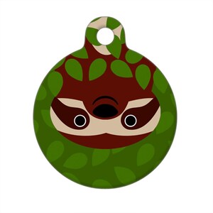 Puede incluir: Una etiqueta redonda verde y marrón para mascotas con la cara de un perezoso de dibujos animados asomando por detrás de hojas verdes.