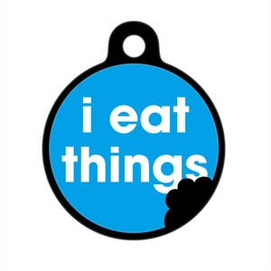 May include: A blue and black dog tag with the text "i eat things" in white letters. A black paw print is partially eaten out of the tag.
