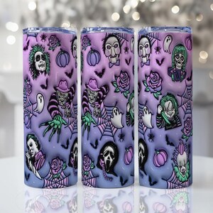 Op de afbeelding: Drie roestvrijstalen bekers met een Halloween-thema. Elke beker heeft een paarse en blauwe gradiënt achtergrond met illustraties van horrorfilmkarakters, geesten, pompoenen en spinnenwebben. De bekers hebben een zilveren deksel.