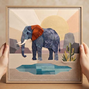 May include: A framed fabric collage artwork featuring a blue elephant with large rust-colored ears standing near a blue water pool. The background displays a desert landscape with a yellow sun, geometric rock formations, and a green cactus.