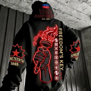 May include: A black hoodie featuring a graphic of a hand holding a flaming torch with broken chains. The back displays the text "FREEDOM'S KEY" and "JUNETEENTH 1865". The hood shows a flag icon and "1865 JUNETEENTH EST. 1865". Sleeves feature red star emblems.