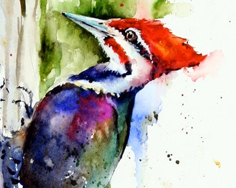 May include: Watercolor painting of a Pileated Woodpecker. The bird features a vibrant red crest, a white and black striped face, and a body with shades of blue, purple, and green. The artwork is set against a backdrop of green foliage and a white background.
