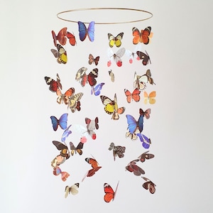Puede incluir: Móvil decorativo con un anillo dorado y numerosas mariposas de papel multicolores. Las mariposas presentan colores vibrantes como rojo, naranja, amarillo, azul y blanco. Ideal para la decoración de interiores y para añadir un toque de fantasía.