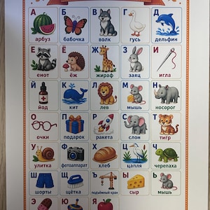 Op de afbeelding: Een rechthoekige educatieve poster met de titel AZBUKA die het Russische alfabet toont. Elke letter is gekoppeld aan een kleurrijke illustratie en een bijbehorend woord in het Cyrillisch, waaronder dieren, voedsel en objecten zoals een raket en camera.