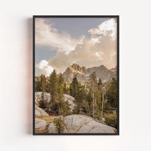 以下が含まれることがあります： 雲の下の山脈を描いた額入りのアートプリント。常緑樹、大きな岩、ベージュ、緑、青の柔らかな色使いのシーンです。アートワークは黒いフレームに表示されます。