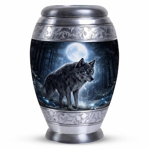 Könnte beinhalten: Silberfarbene Urne mit Wolfsmotiv. Die Urne zeigt einen schwarzen Wolf mit blauen Augen in einer mondbeschienenen Waldszene. Dekorative Muster zieren die oberen und unteren Ränder.