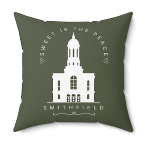 May include: Square decorative pillow with a dark olive green background. The pillow features a white illustration of a building with the text "SWEET IS THE PEACE" arched above and "SMITHFIELD" below. The design includes hearts.