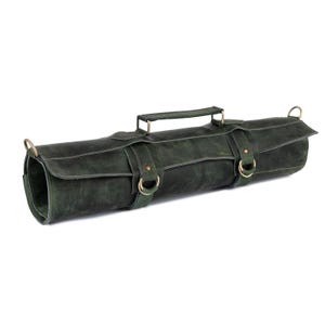 Könnte beinhalten: Eine dunkelgrüne Leder-Messertasche mit Griff und messingfarbener Hardware. Die Rolle hat zwei Riemen mit Schnallen und Metallringen zur Befestigung eines Schultergurts. Das Leder hat ein Used-Look-Aussehen.