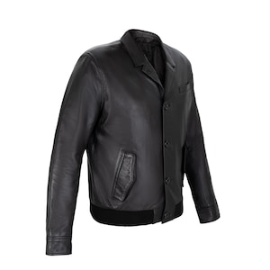 May include: A black leather jacket featuring a pointed collar, a front button closure with four visible buttons, two slanted side pockets, and a ribbed black hem. The jacket has long sleeves with buttoned cuffs and a smooth, matte leather finish.