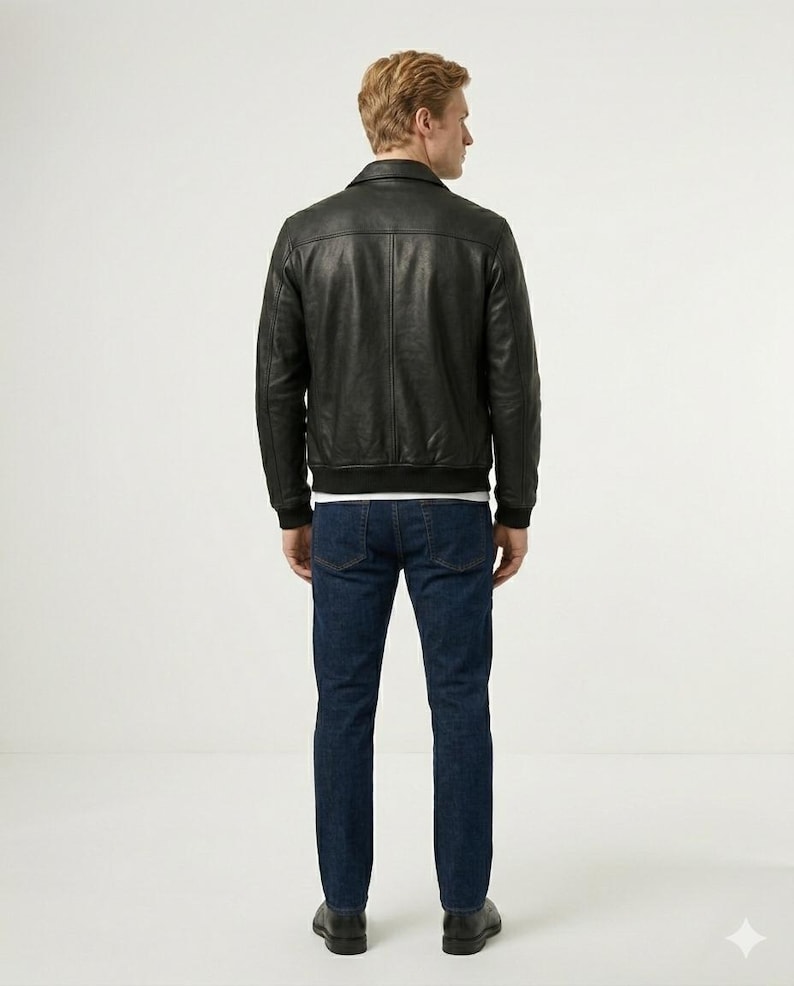 May include: A black leather jacket with a classic collar, long sleeves, and a ribbed hem, paired with dark blue denim jeans. The jacket features a smooth texture and visible vertical seam detailing on the back, worn over a plain white shirt.