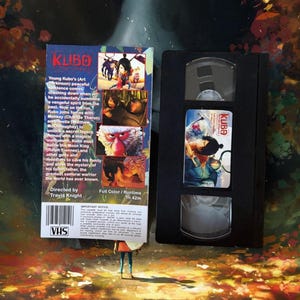 May include: A VHS tape and its cover for the animated film "Kubo and the Two Strings." The cover features colorful illustrations of characters and scenes from the movie. The VHS tape is black with a label showing Kubo. The runtime is 1 hour and 42 minutes.