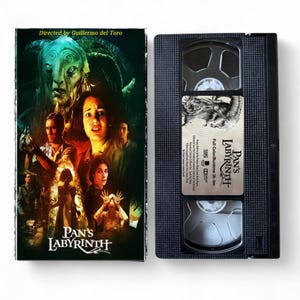 Puede incluir: Una cinta VHS y su carátula de la película "El laberinto del fauno". La carátula presenta una criatura fantástica y varios personajes humanos. La cinta negra tiene una etiqueta con el título de la película y un gráfico.