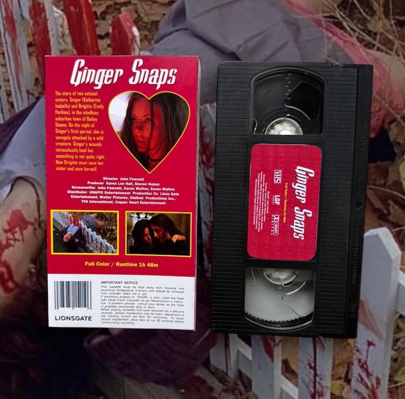 Puede incluir: Una cinta VHS y su estuche de la pel&iacute;cula de terror "Ginger Snaps". El estuche es rojo con el t&iacute;tulo de la pel&iacute;cula en una fuente estilizada y una imagen en forma de coraz&oacute;n de dos mujeres. La cinta VHS es negra con una etiqueta roja.
