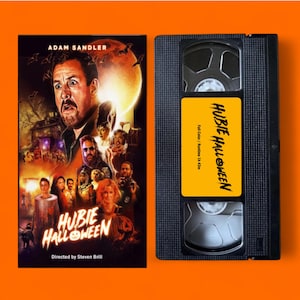 Op de afbeelding: Een VHS-band en filmposter voor de film "Hubie Halloween" met Adam Sandler. De poster toont een cast van personages tegen een spookachtige achtergrond. De VHS-band heeft een geel label met de filmtitel.