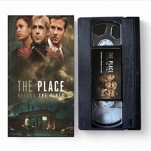Może przedstawiać: Czarna kaseta VHS i jej okładka do filmu "The Place Beyond the Pines". Okładka przedstawia aktorów i tytuł filmu. Etykieta kasety również wyświetla tytuł i aktorów filmu.