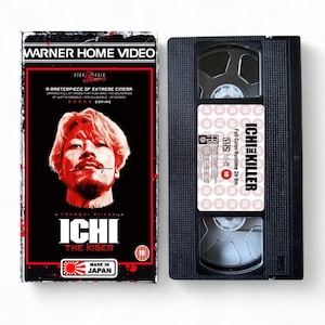 May include: A black VHS tape and case for the movie "Ichi the Killer." The case features a red and black design with the film's title and a portrait of a man. The tape itself is black with a white label.