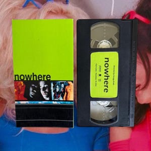 May include: A VHS tape and its case for the film "Nowhere." The case is lime green with the movie title and a cast photo. The VHS tape is black with a green label bearing the movie title.