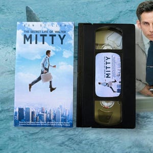 以下が含まれることがあります： ベン・スティラー主演の映画「The Secret Life of Walter Mitty」のVHSテープと映画カバー。カバーには、都市の上を走る男性が描かれています。VHSテープは黒色で、映画のタイトルと走る人物が描かれたラベルが付いています。
