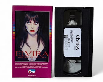 May include: A VHS video cassette and its case for the film "Elvira: Mistress of the Dark." The case is magenta with the movie title and a portrait of Elvira. The VHS tape is black with a white label.