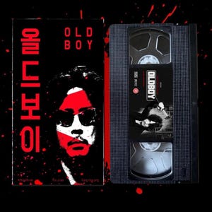 Könnte beinhalten: Eine VHS-Kassette und Hülle für den Film "Oldboy". Die Hülle zeigt ein stilisiertes Bild eines Mannes mit Sonnenbrille und roten und weißen Akzenten. Das Band selbst trägt den Filmtitel und eine Szene.