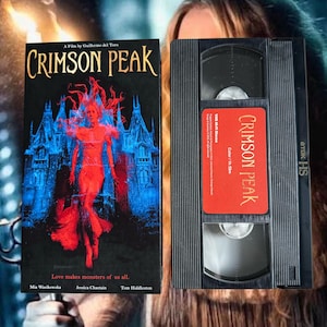 Könnte beinhalten: Eine Crimson Peak VHS-Kassette mit Hülle. Das Cover zeigt eine rote Figur vor einem blauen gotischen Herrenhaus mit dem Text 'Crimson Peak' und 'Love makes monsters of us all.' Die Kassette hat ein rotes Etikett mit der Aufschrift 'Crimson Peak'.