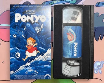 May include: A VHS tape and its cover for the animated film "Ponyo." The cover is predominantly blue, with the title in white and an illustration of a girl. The black VHS tape has a label with the film's title and artwork.
