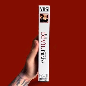 Puede incluir: Una cinta VHS blanca de la pel&iacute;cula "El diablo viste de Prada". La cinta tiene una peque&ntilde;a imagen del elenco en la parte superior y el t&iacute;tulo de la pel&iacute;cula en rojo y blanco. Tambi&eacute;n muestra los logotipos "hi-fi" y "Dolby Digital".
