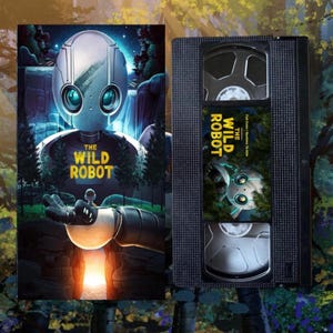 May include: A VHS tape with the film "The Wild Robot." The cover art shows a silver robot with blue eyes, set against a forest and waterfall. The title is in yellow and white text.