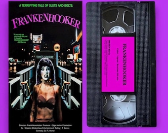 Könnte beinhalten: Eine VHS-Kassette und ihre Hülle für den Film "Frankenhooker" werden vor einem lila Hintergrund gezeigt. Die Hülle zeigt eine Frau in einem BH vor dem Times Square. Die Kassette hat ein pinkfarbenes Etikett mit dem Filmtitel.