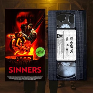 Puede incluir: Una cinta VHS y un cartel de la película "Sinners". El cartel presenta una ilustración dramática y colorida de personas y una guitarra. La cinta VHS es negra con una etiqueta blanca que dice "Sinners".