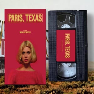 Op de afbeelding: Een rode VHS-band en filmhoes voor de film "Paris, Texas" van Wim Wenders. De hoes toont een vrouw met blond haar en de filmtitel in gouden letters. De VHS-band heeft een bijpassend label.