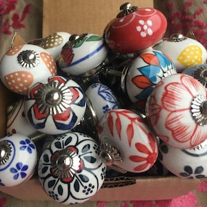 Peut inclure: Un assortiment de boutons de meubles en céramique décoratifs. Les boutons présentent des motifs floraux, à pois et géométriques en rouge, bleu, orange et blanc. Chaque bouton a une base en métal argenté.