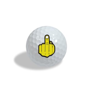 Puede incluir: Pelota de golf blanca con un gráfico amarillo y negro de una mano mostrando el dedo medio. La pelota tiene una superficie con hoyuelos y está diseñada para jugar al golf.