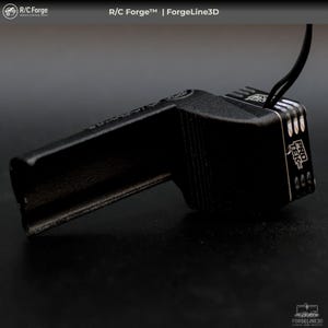 May include: Black, angular electronic component with the text "PRO TEK" and "R/C Forge" printed on it. The component has a series of parallel lines and a wire extending from it. The background is dark.