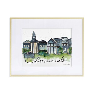 Puede incluir: Pintura a la acuarela enmarcada de un paisaje urbano. La obra representa edificios en tonos azules y verdes, con la palabra "hernando" en cursiva. La pintura está sobre un fondo blanco y enmarcada en oro.