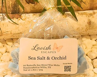 Puede incluir: Una bolsa de plástico transparente con 20 ceras aromáticas de soja de color azul claro en forma de mariposa. La etiqueta dice Lavish Escapes, Sea Salt & Orchid, 20 Butterfly Soy Blend Wax Melts, Handcrafted in Willis, TX, 50g, e incluye un código QR.
